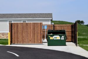a wooden privacy fence built around a trash receptacle with the gates open