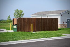 a wooden privacy fence built around a trash receptacle with the gates open