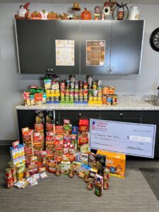 a large check with seated next to food pantry donations